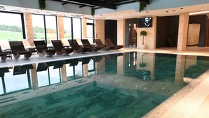 Une piscine intérieure moderne, dotée de chaises longues et offrant une vue sur l’extérieur.