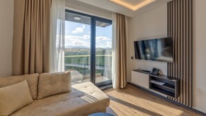 Une chambre d’hôtel moderne dotée d’un canapé, d’une télévision à écran plat, d’une porte-fenêtre coulissante donnant sur un balcon et d’un plancher en bois.