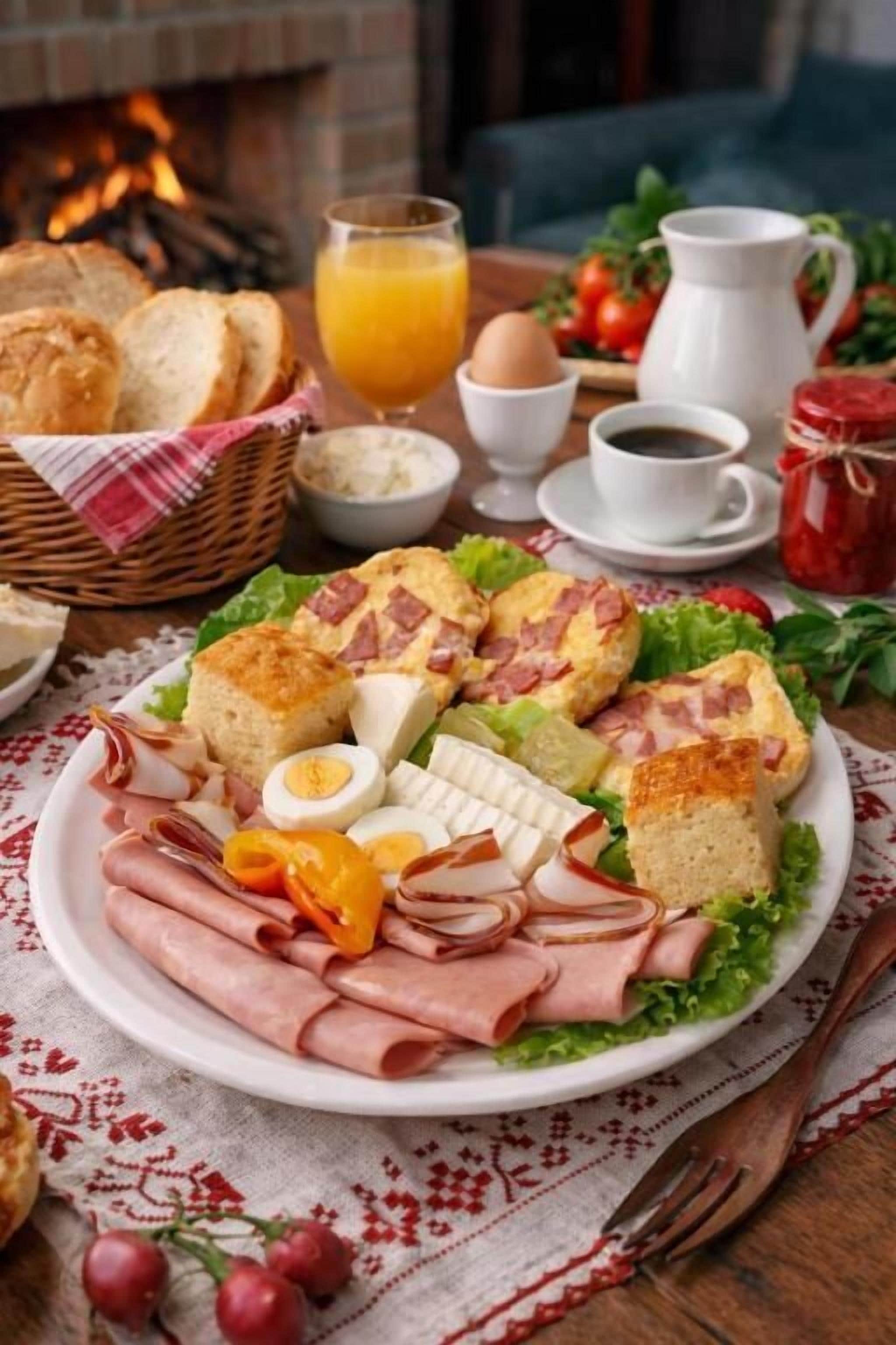 A breakfast plate with various foods, a glass of orange juice, and a coffee cup on a table with a fireplace in the background.