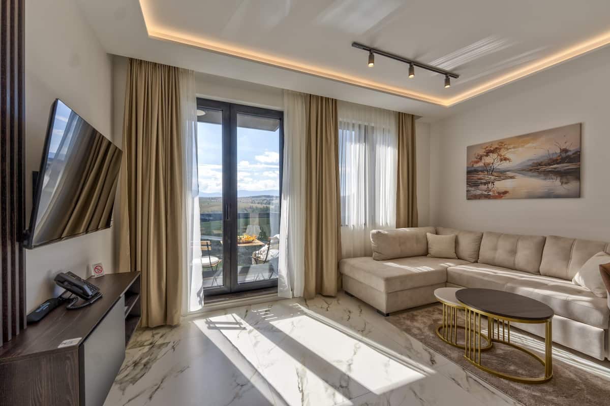A modern living room with a sectional sofa, a round coffee table, a flat-screen TV, and a balcony with a view.