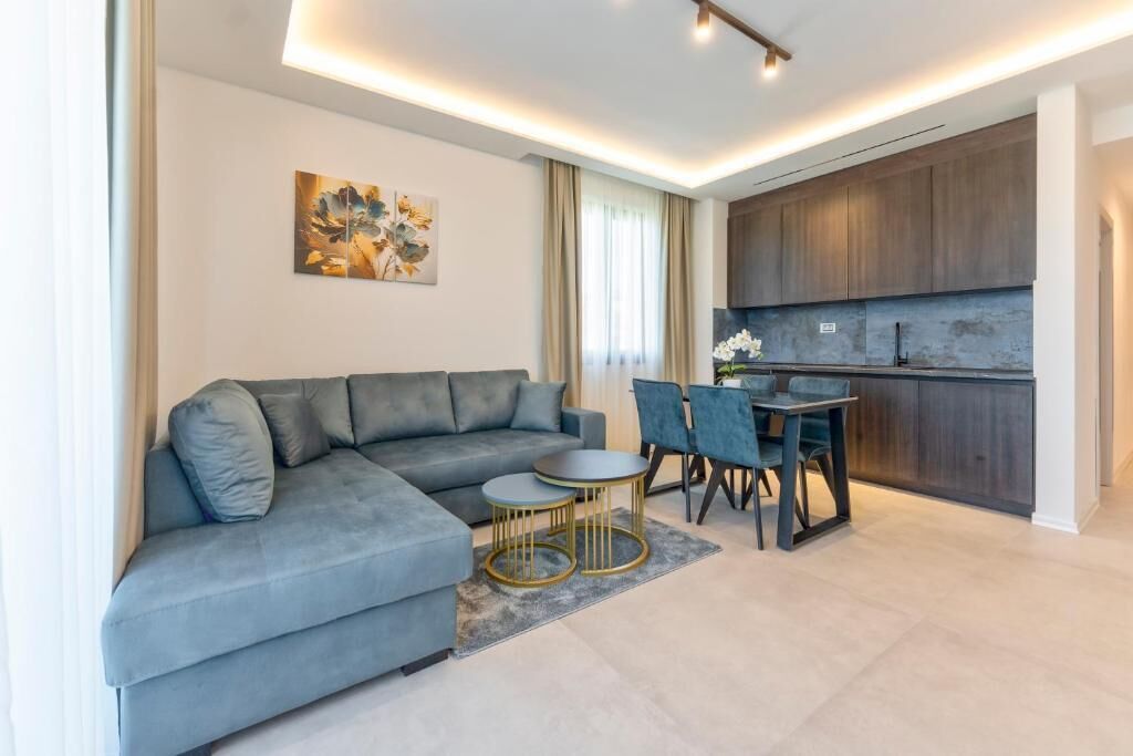 Un salon moderne avec un canapé gris, une table à manger avec des chaises et un coin cuisine doté de meubles en bois.