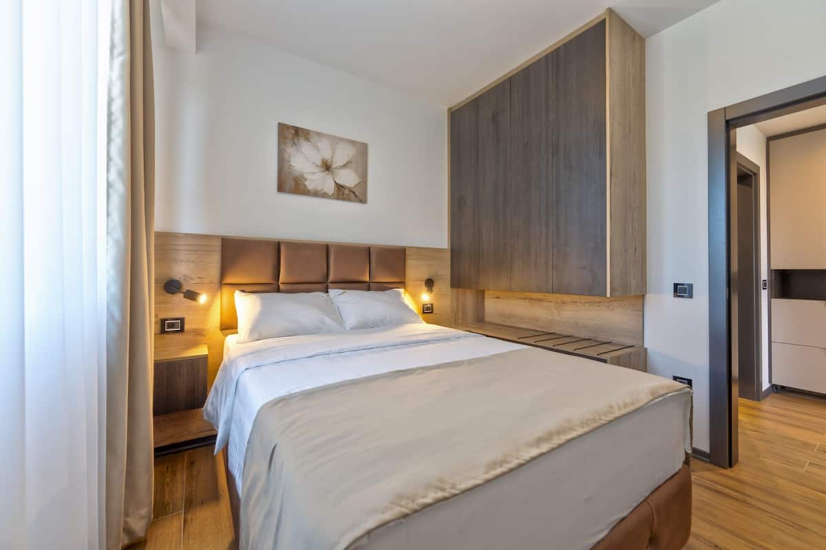 A neatly arranged hotel room with a bed, bedside lamps, a wall-mounted artwork, and a wooden headboard.