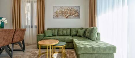 Una sala de estar con un sofá verde, dos mesas redondas, una mesa de comedor con sillas y una obra de arte en la pared.