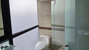 Un baño moderno con cabina de ducha de vidrio, inodoro y lavamanos con encimera de vidrio.