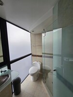 A modern bathroom with a glass shower enclosure, a toilet, and a sink with a glass countertop.