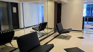 Un área de espera moderna con sillas negras, un panel de vidrio y piso de baldosas.