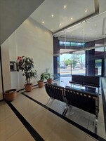 A modern lobby with a reception desk, potted plants, and a glass partition.