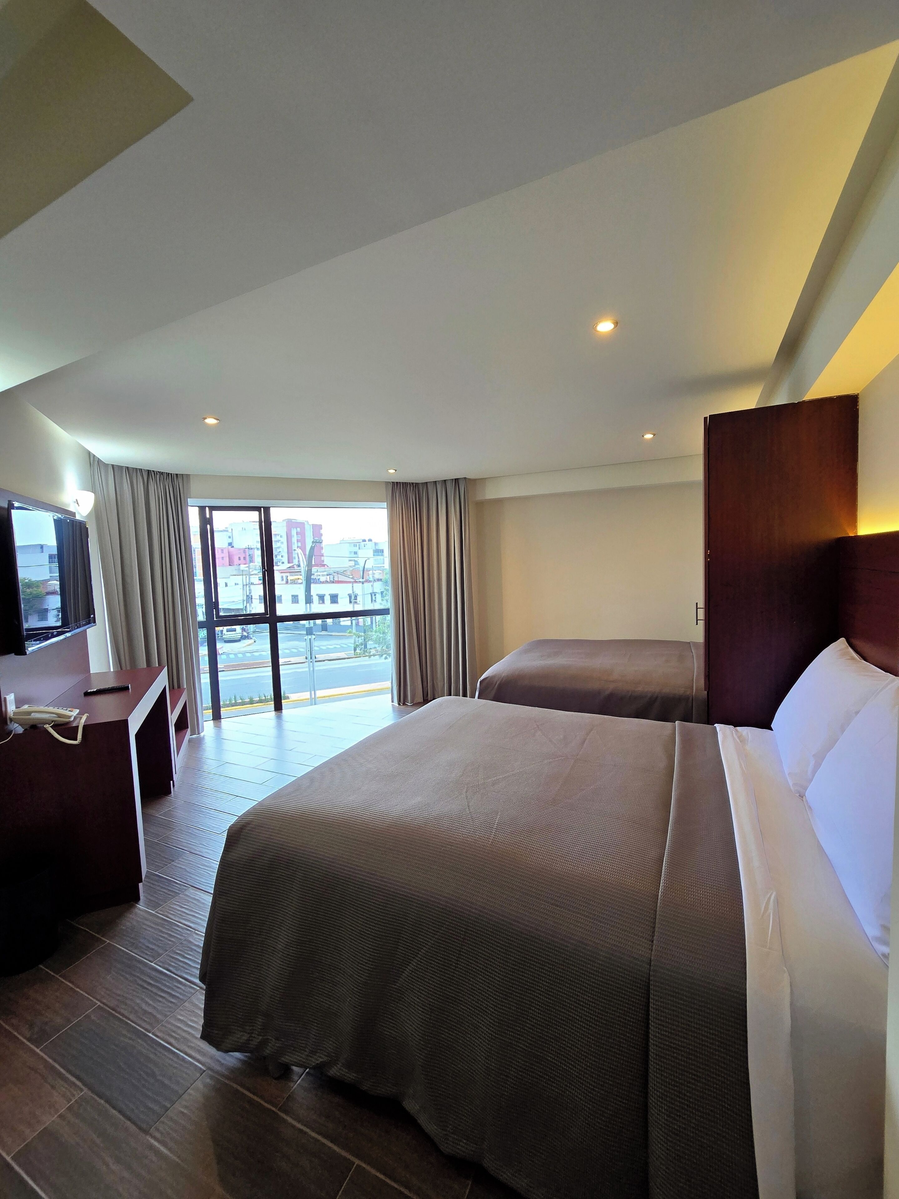 A hotel room with a large bed, a desk with a telephone, and a TV.