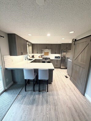 Una cocina moderna con una isla central, dos taburetes de bar, horno empotrado y refrigerador.