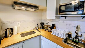 A compact kitchen with a microwave, toaster, kettle, and a sink.