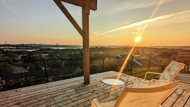 A wooden deck with a table and two chairs, overlooking a bridge and landscape.