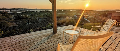 Une terrasse en bois avec une table et deux chaises, d’où l’on peut admirer un pont et le paysage environnant.