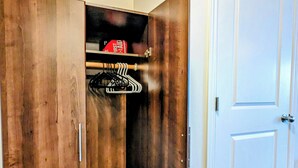 A walk-in closet with a wooden wardrobe, a hanging rack, and a folded ironing board.