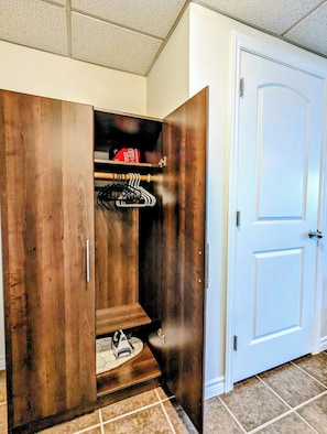 Un dressing accessible sans porte, avec une armoire en bois, une tringle à vêtements et une planche à repasser pliante.