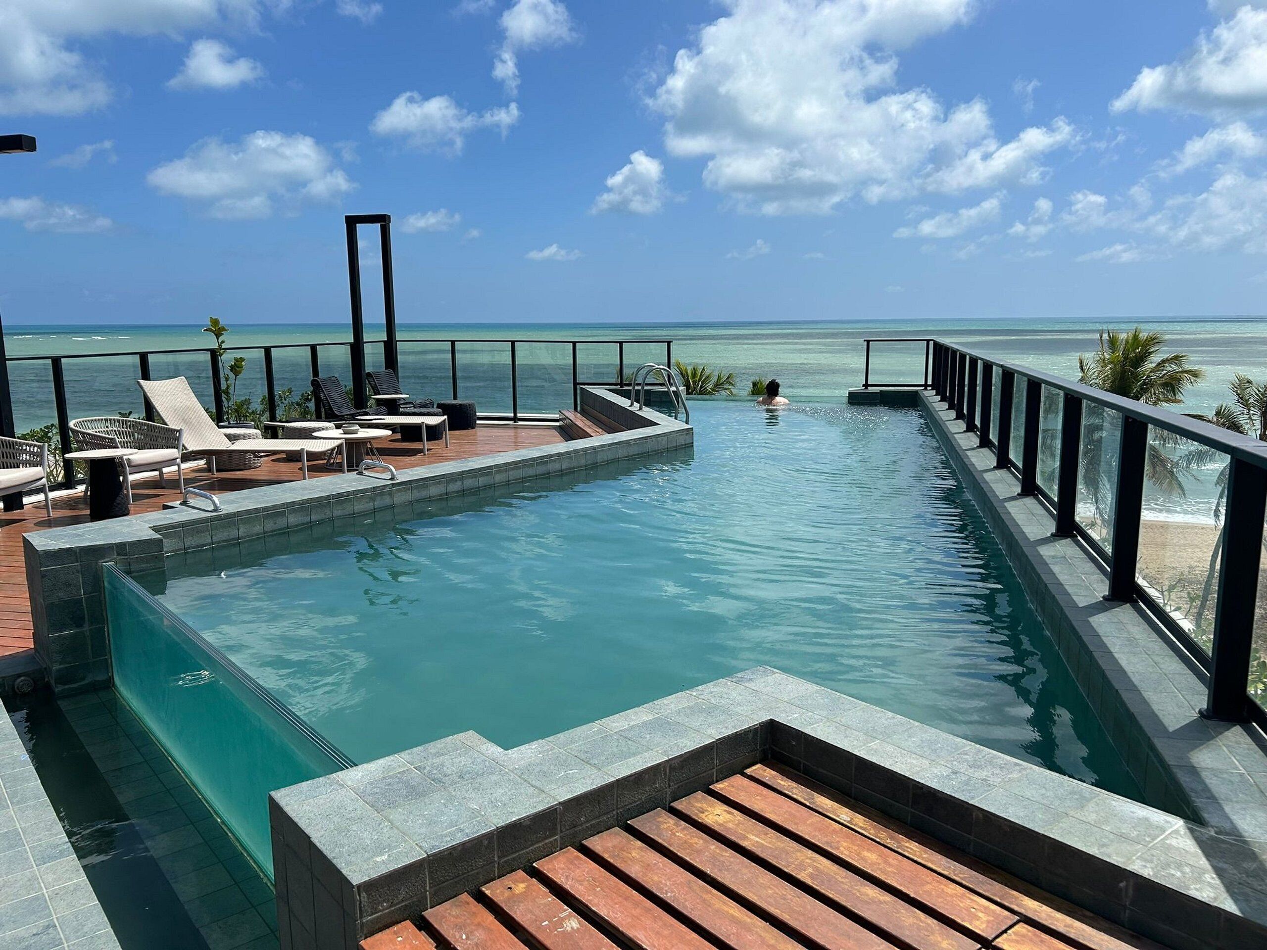 A pool with a view of the ocean, lounge chairs, and a wooden deck.