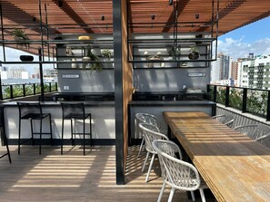 Eine Dachterrasse mit Holztisch und -stühlen, einem Metallgeländer und Blick auf die Stadt.