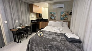 Una habitación de hotel compacta con cama, escritorio, kitchenette y zona de ducha.