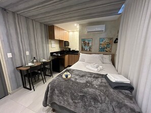 Ein kleines Hotelzimmer mit Bett, Schreibtisch, einer Küchenzeile und einer Duschkabine.