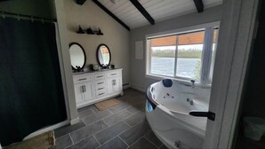 A bathroom with a bathtub, a vanity with a mirror, and a window with a view of a body of water. - Jerry's Lake House Unit 1 on Denise Lake, Soldotna (Soldotna)