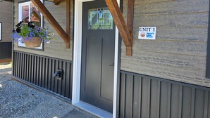 A building entrance with a wooden overhang, a door labeled 'UNIT 1,' and a hanging flower basket. - Jerry's Lake House Unit 1 on Denise Lake, Soldotna (Soldotna)