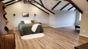 A bedroom with a bed, a wooden floor, a ceiling fan, and a view of an adjacent room. - Jerry's Lake House Unit 1 on Denise Lake, Soldotna (Soldotna)