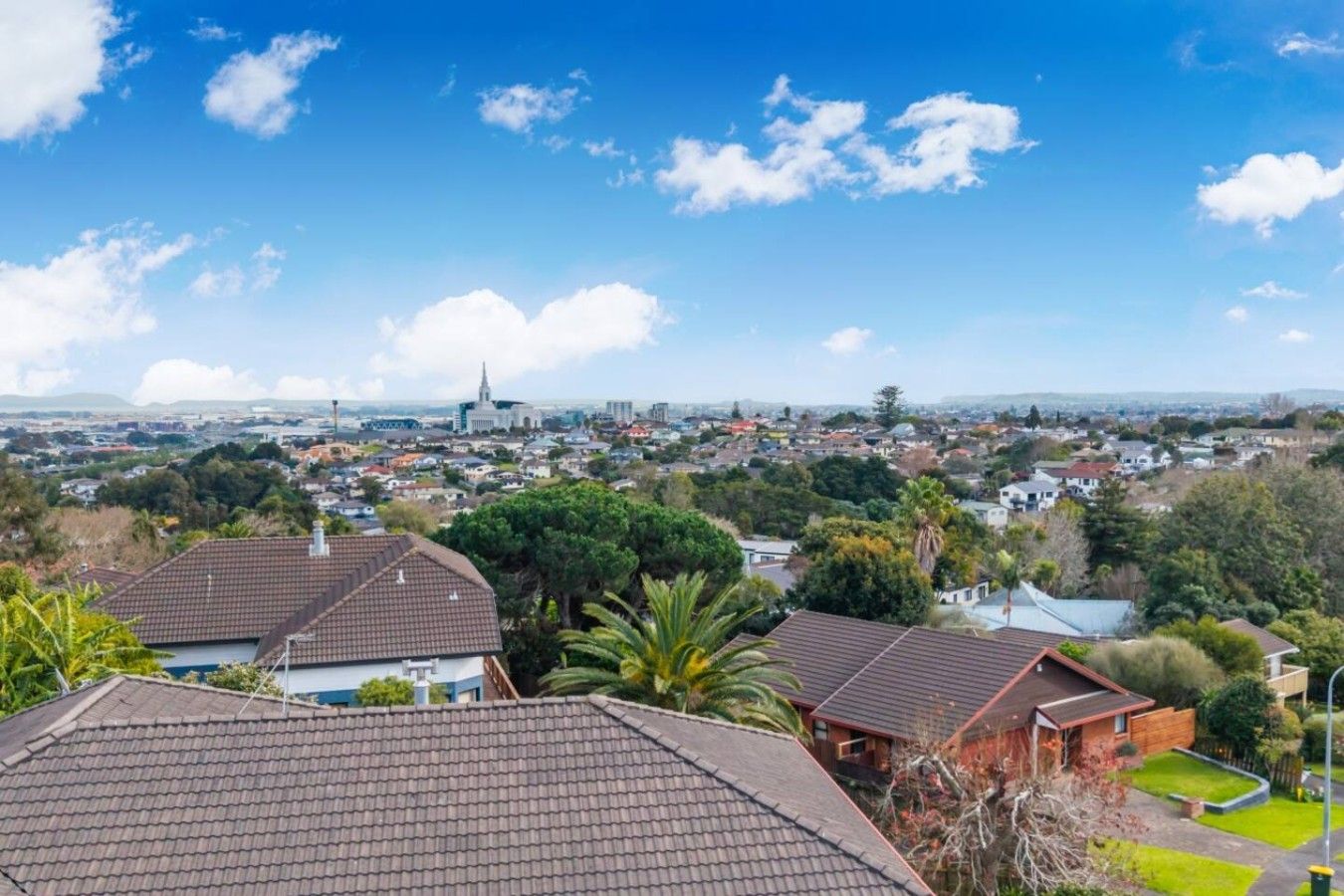Un quartier résidentiel avec des maisons, un bâtiment imposant visible au loin et un ciel dégagé.