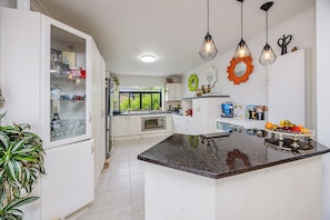 A modern kitchen with white cabinets, a granite countertop, and pendant lighting. - Spacious 5BR Holiday Home Near Manukau (Goodwood Hights)