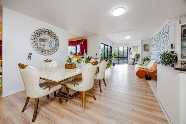 A modern dining area with a marble table, white chairs, and a decorative mirror on the wall.