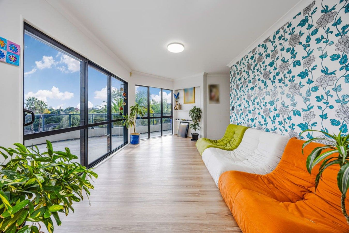 Uma sala de estar moderna com uma janela grande, um sofá com almofadas laranja e uma parede estampada.