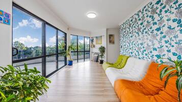 Uma sala de estar moderna com uma janela grande, um sofá com almofadas laranja e uma parede estampada.