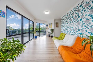 Una sala moderna con un ventanal grande, un sofá con cojines anaranjados y una pared con diseño.