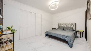 Une chambre à coucher comprenant un lit, une table de chevet, une tête de lit fixée au mur, une porte et un luminaire au plafond.
