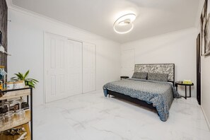 A bedroom with a bed, a nightstand, a wall-mounted headboard, a door, and a ceiling light fixture. - Spacious 5BR Holiday Home Near Manukau (Goodwood Hights)