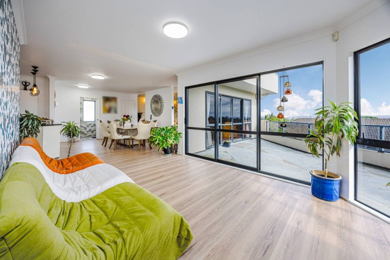 A spacious living area with a large window, a dining area, and a balcony with plants.
