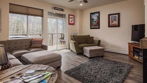 A living room with a sofa, ottoman, coffee table, and a television. There is a ceiling fan, a fireplace, and a door labeled 'Waterfall.' - Girdwood Mountain Basecamp-Sleeps 7-Near Alyeska (Anchorage)