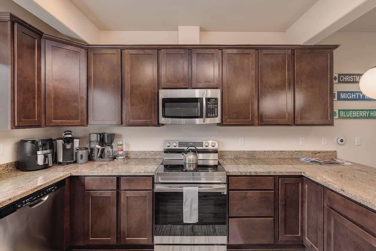 A kitchen with dark wood cabinets, stainless steel appliances, a granite countertop, and a dishwasher.