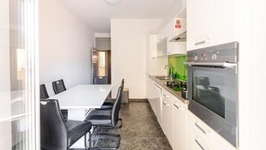 A modern kitchen with a white countertop, stainless steel appliances, and a dining area with a white table and black chairs. - Perfect 2-bedroom apartment with AC in charming Split (Split)