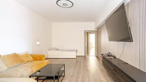 A modern living room with a sofa, a coffee table, a flat-screen TV mounted on the wall, and a bed in the background. - Perfect 2-bedroom apartment with AC in charming Split (Split)
