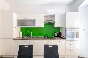 Une cuisine moderne avec des meubles blancs, un plan de travail vert, un évier, une cuisinière et deux chaises.