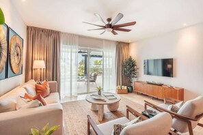 A modern living room with a ceiling fan, a television, and a sliding glass door leading to an outdoor area. - AEA - Punta Palmera (Punta Cana)