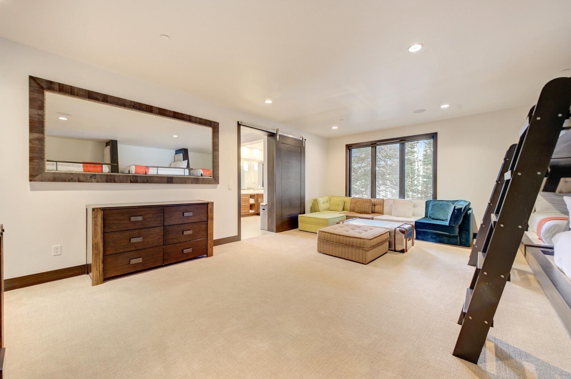 A spacious living room with a large mirror, a wooden cabinet, a sofa, a coffee table, and a staircase.