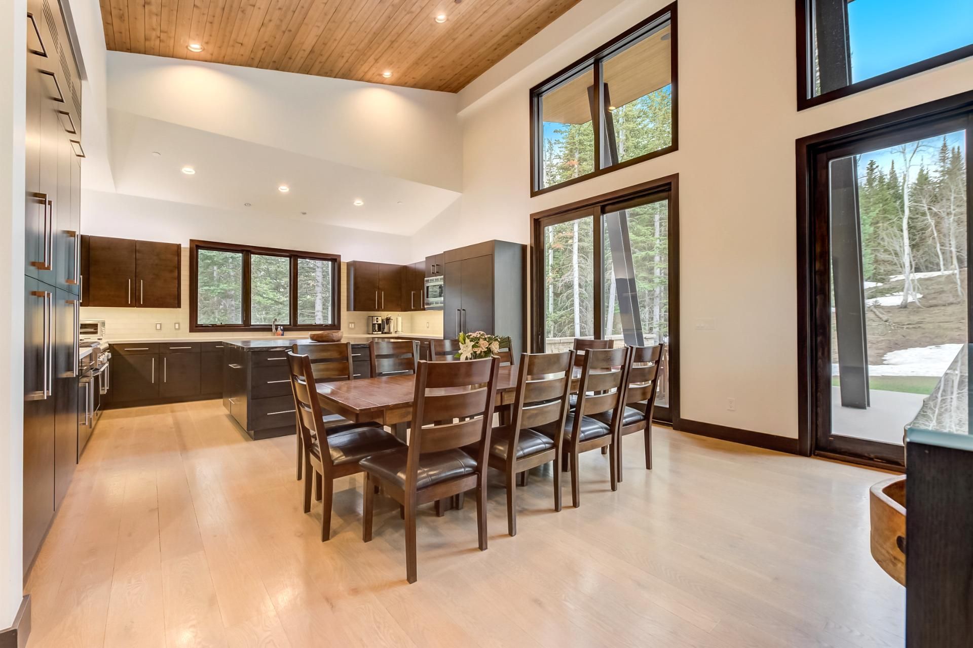 A modern kitchen with dark wood cabinets, a central island, and a dining area with wooden chairs.
