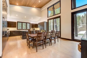 A modern kitchen with dark wood cabinets, a central island, and a dining area with wooden chairs. - KBM Resorts | Walk to Slopes, Sports Court, Private Home Theater, Sleeps 16, Private Hot Tub PCO-184G (Park City)