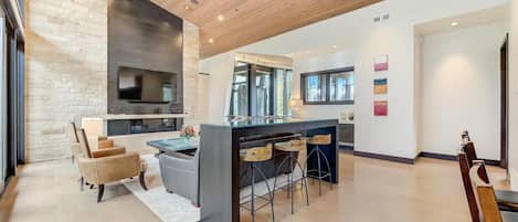 A modern kitchen with a large island, bar stools, and a flat-screen TV mounted on a stone wall.