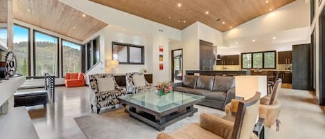 A spacious living area with a high ceiling, large windows, and a modern kitchen.