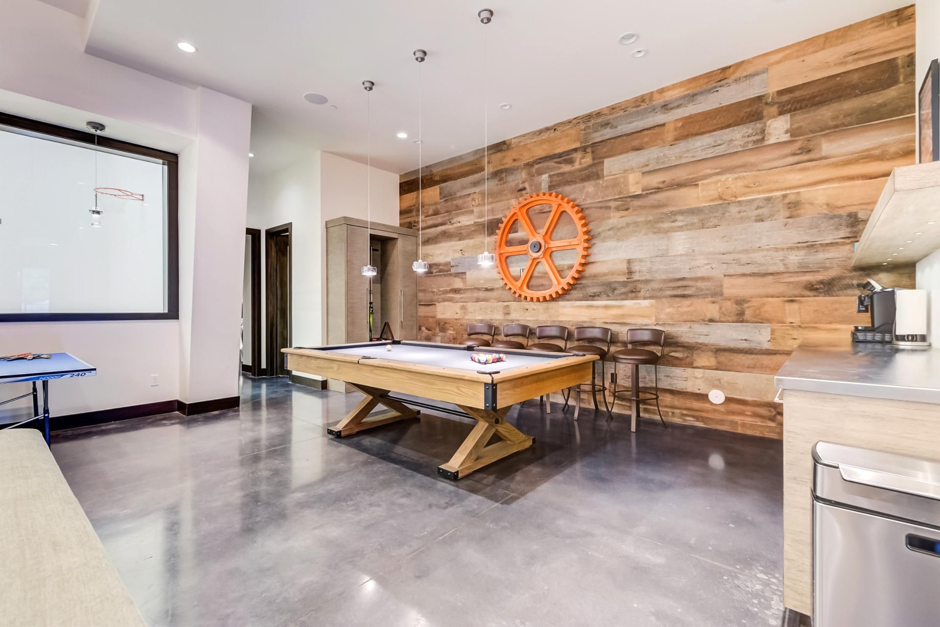 A billiards table with chairs, a projector screen, and a coffee machine in a modern room with wooden wall panels.