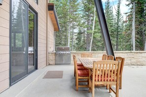 An outdoor dining area with a table and chairs, a grill, and a stone wall. - KBM Resorts | Walk to Slopes, Sports Court, Private Home Theater, Sleeps 16, Private Hot Tub PCO-184G (Park City)