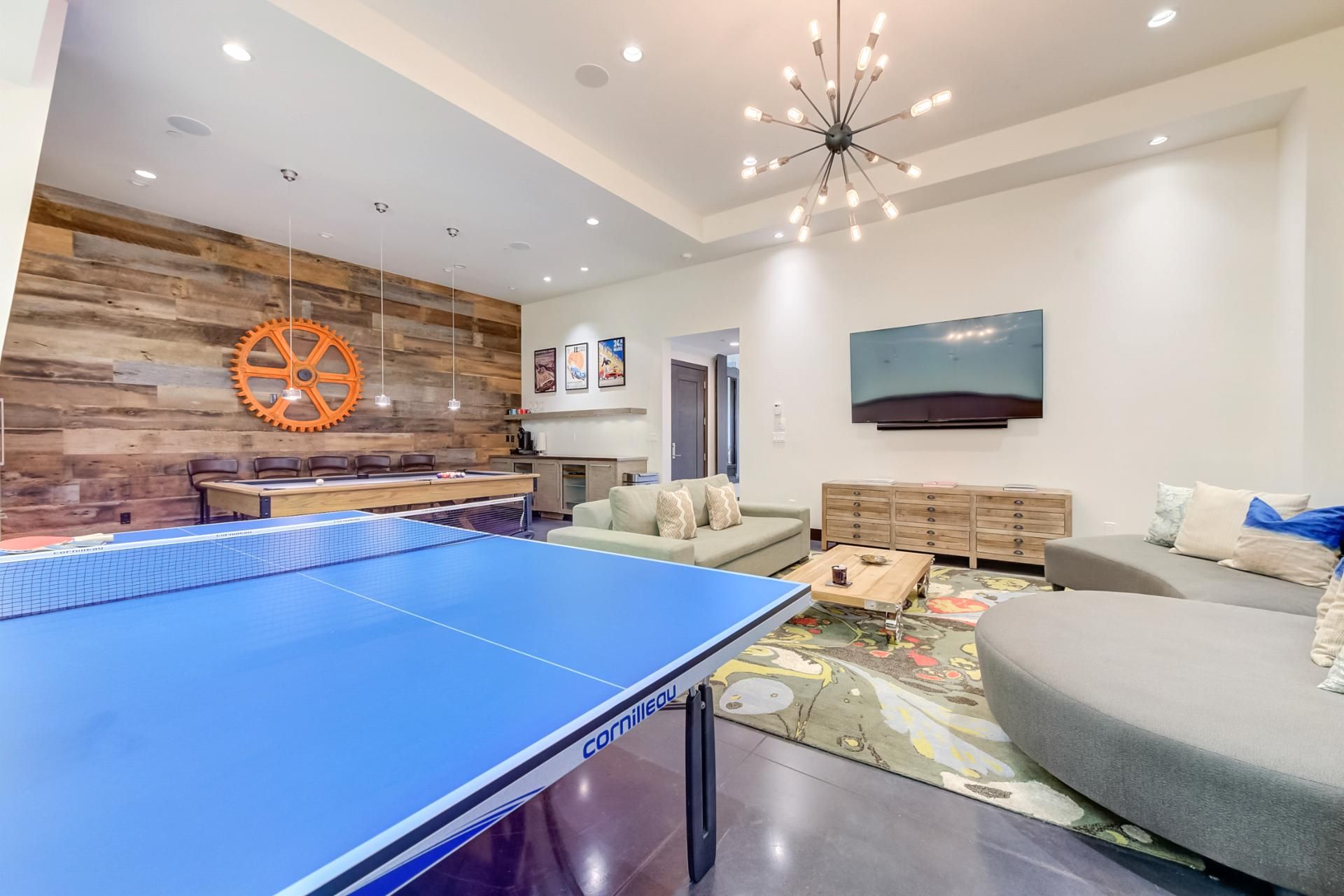 A modern living room with a ping pong table, a sofa, a TV, and a wooden wall with a gear decoration.