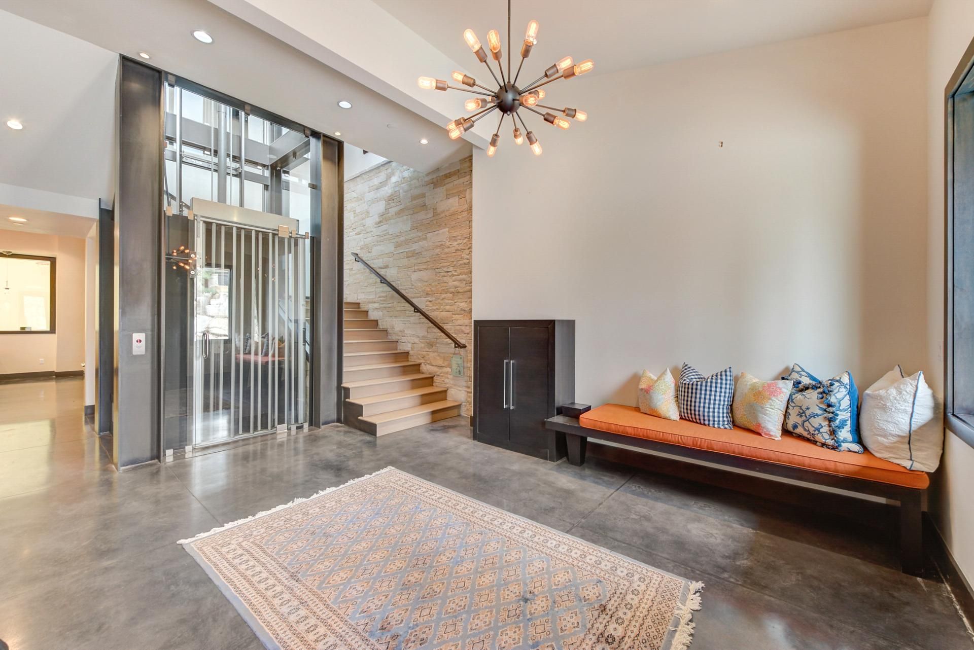 A modern interior with a staircase, a seating area with cushions, and a patterned rug.