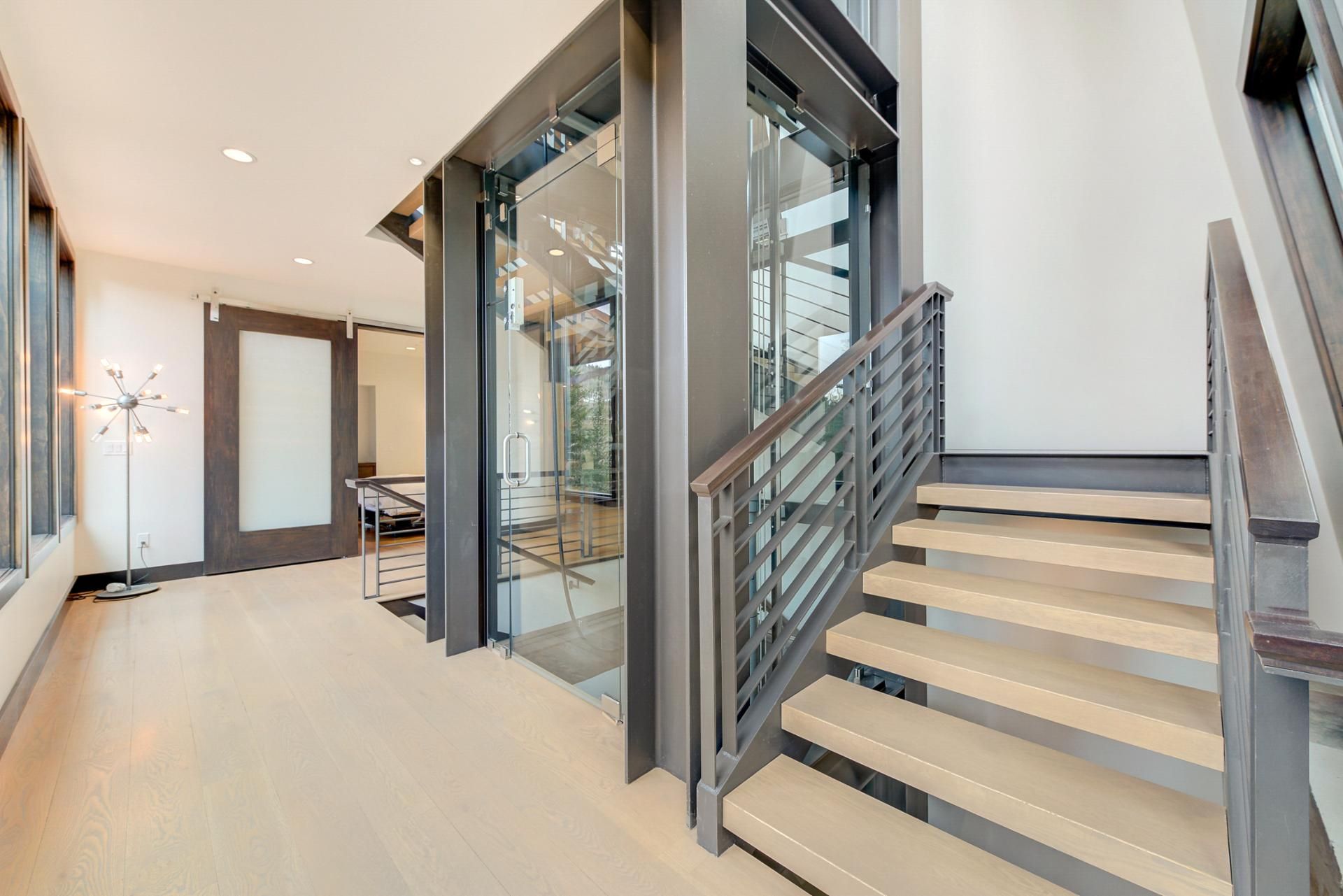 Un interior moderno con una escalera, puertas de cristal y una lámpara de pie.